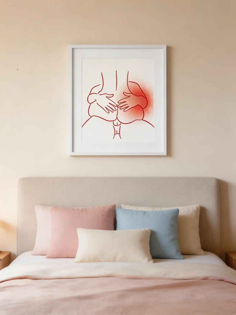 May include: A framed art print featuring a red line drawing of two figures embracing. The artwork is displayed above a bed with pink, blue, and cream-colored pillows. The bedspread is a soft pink.