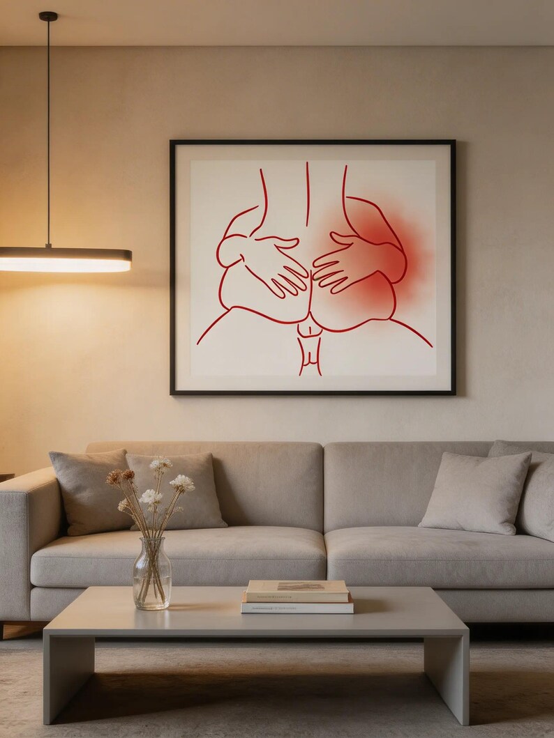 May include: A framed art print featuring a minimalist line drawing in red. The artwork depicts a stylized representation of two figures in an intimate embrace. The background is a neutral beige, and the frame is black.
