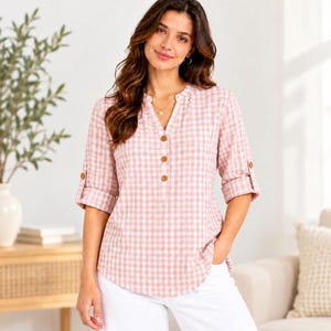 Puede incluir: Una blusa con estampado de cuadros vichy en rosa claro y blanco que presenta un escote en V, una parte frontal con tres botones marrones y mangas tres cuartos con trabillas abotonadas en los puños, combinada con pantalones blancos.