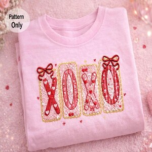 Op de afbeelding: Een lichtroze t-shirt met de geborduurde letters "XOXO" in rood en wit, versierd met kleine hartjes en strikjes. Het ontwerp is omlijst met een gouden rand en een geschulpte kantachtige rand. De woorden "Pattern Only" staan in de linkerbovenhoek.
