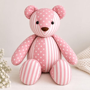 May include: A stuffed teddy bear constructed from fabric featuring a patchwork design of pink and white polka dots and vertical stripes. The bear has two round black eyes and a brown nose, with a seated posture and rounded limbs and ears.