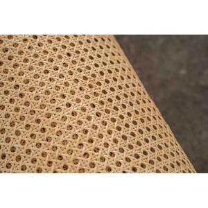 May include: Close-up of a woven rattan material with a repeating pattern of small, evenly spaced holes. The natural beige color of the rattan is visible, with a slight variation in tone. The texture is intricate and detailed, suggesting a handcrafted item.