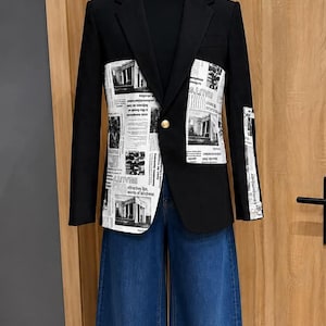 Peut inclure: Un blazer noir avec des panneaux blancs imprimés de motifs de journaux en noir et blanc sur le devant et la manche, porté sur un haut noir à col montant et un jean bleu large. Le blazer possède un bouton doré unique au centre.