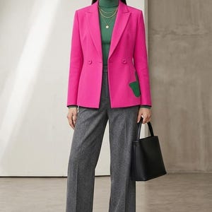 Peut inclure: Un blazer rose vif à double boutonnage avec un détail de poche vert, porté sur un pull à col roulé vert et un pantalon gris. La tenue comprend un sac à main noir et des bottines noires, accessoirisée avec des colliers dorés et des créoles.