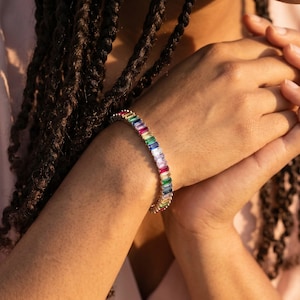 Puede incluir: Una pulsera plateada con piedras preciosas rectangulares y coloridas. La pulsera presenta un arcoíris de colores, incluyendo rojo, naranja, amarillo, verde, azul y morado. Las piedras están dispuestas en fila, creando un accesorio vibrante.