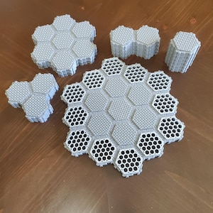May include: A collection of gray, hexagonal tiles with a textured surface and honeycomb-patterned cutouts. The tiles are arranged in various configurations, suggesting a modular design or puzzle pieces.