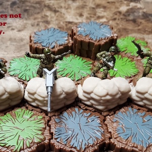 May include: Miniature military figures on a hexagonal game board with terrain features. The figures are dressed in green uniforms and are positioned near beige cloud-like structures. The board has brown, green, and blue sections. Text reads: "Additional figures/hexes not included. For display only."