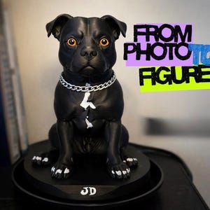 Puede incluir: Una figura de perro negro con ojos naranjas, un collar de cadena plateada y marcas blancas en el pecho y las patas. La base presenta las letras JD. El texto a la derecha dice FROM PHOTO TO FIGURE. El perro está sentado sobre una base redonda.