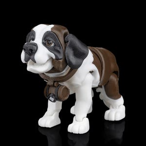 Op de afbeelding: Een 3D-geprint beeldje van een Sint-Bernardhond in staande houding. De hond heeft een bruin-witte vacht, met zwarte accenten op de oren en neus. Hij draagt een bruine halsband met een klein vat. Zwarte achtergrond.