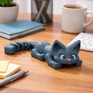 May include: A dark gray cat-shaped desk organizer with blue eyes and a pink nose, lying on a wooden desk. The cat's tail is segmented. Other desk items include a notepad, pen, and a cup of coffee.