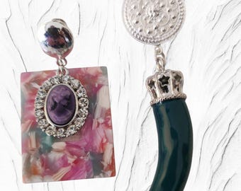 May include: A pair of earrings. One earring has a rectangular pendant with a floral pattern and a cameo. The other earring features a silver crown and a dark green horn-shaped pendant.