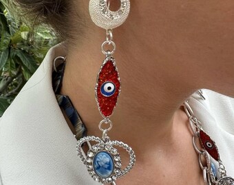 May include: Silver dangle earrings with a red evil eye charm, a white cameo charm, and a round silver charm with rhinestones.