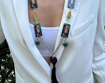 May include: A long necklace with rectangular pendants featuring a Frida Kahlo portrait, interspersed with decorative elements. The necklace has a black beaded chain, silver-tone metal accents, and a black tassel.