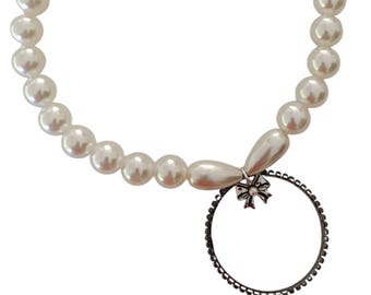 May include: A white pearl necklace with a silver toggle clasp. The necklace features large, round pearls and a decorative pendant with a bow and a circular frame. The necklace is a statement piece.