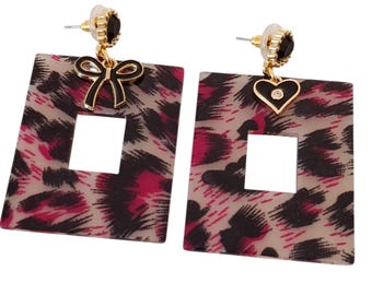 May include: A pair of square drop earrings featuring a leopard print pattern in pink, black, and beige. Each earring has a square cut-out and is decorated with a gold-coloured bow or heart charm. The earrings have gold-coloured posts.