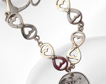 May include: Silver-toned bracelet featuring infinity symbols with heart cutouts. A round charm with an eye design hangs from the bracelet. The bracelet has a lobster clasp closure.