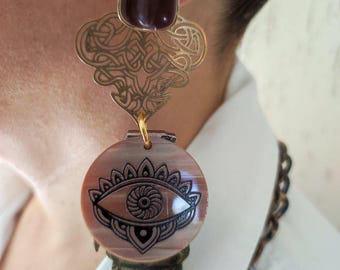 May include: Gold and brown statement earrings with a dark brown stone at the top and a round, shell-like pendant with a black eye design.
