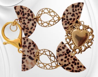 May include: A gold bracelet with leopard print details and a heart-shaped charm. The bracelet has a lobster clasp and decorative gold links. The leopard print is a mix of beige and dark brown.