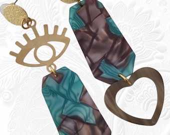 May include: A pair of drop earrings. One earring features a gold-coloured eye design, while the other has a heart shape. Both earrings have a gold-coloured stud and a rectangular pendant with teal and brown marbled patterns.