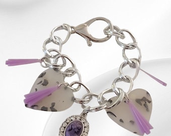 May include: Silver bracelet with heart-shaped charms, a cameo pendant, and purple details. The bracelet has a chain link design and a lobster clasp. The heart charms have a speckled pattern.