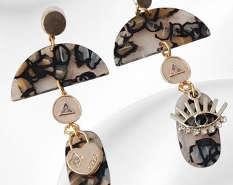 May include: A pair of dangle earrings with a marbled pattern in black, white, and tan. Each earring features a gold-toned half-circle, a triangle pendant, and a heart-shaped charm with the word "LOVE". One earring has an eye-shaped charm.
