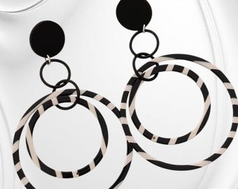 May include: A pair of black and white hoop earrings. Each earring has a black circular stud, connected to two black rings and a larger hoop with a black and white striped pattern. A striking, geometric accessory.
