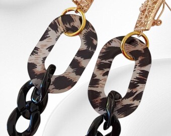 May include: Dangle earrings with gold-coloured textured rectangular studs. The earrings feature a chain design with oval links in a leopard print pattern, connected to black oval links, creating a bold statement.