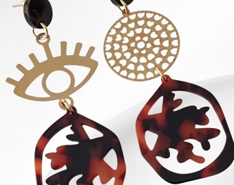 May include: A pair of dangle earrings with a gold-tone eye design and a tortoise shell-patterned pendant. The earrings also feature a gold-tone circle with cut-out details and a black circular stud.