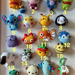 May include: A collection of twenty small, crocheted yarn keychains featuring various colorful characters and animals, each numbered from 1 to 20. The items include figures like a yellow bear, a pink pig, a blue creature, a green frog, and others.