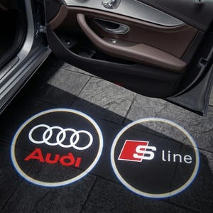 May include: Car door projection lights displaying the Audi logo and the S line emblem. The Audi logo features white interlocking rings and the word "Audi" in red. The S line emblem has a red "S" and the text "line" in white.