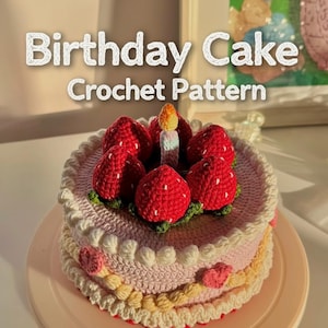 Op de afbeelding: Een gehaakte verjaardagstaart met rode aardbeienversieringen en een brandende kaars. De taart heeft meerdere lagen met roze, gele en witte glazuurdetails. De tekst "Birthday Cake Crochet Pattern" staat bovenaan.