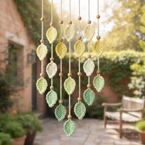 Op de afbeelding: Decoratieve bladgordijn met gehaakte bladeren in tinten geel en groen, opgehangen aan koorden met houten kralen. De bladeren zijn in een trapsgewijs patroon gerangschikt, wat een decoratief accent creëert.