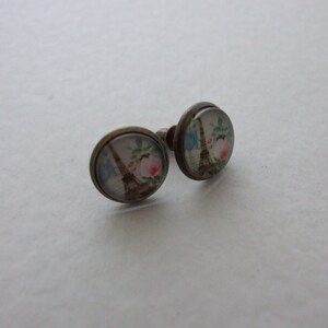 May include: A pair of bronze stud earrings with a glass cabochon featuring a vintage illustration of the Eiffel Tower with pink flowers.