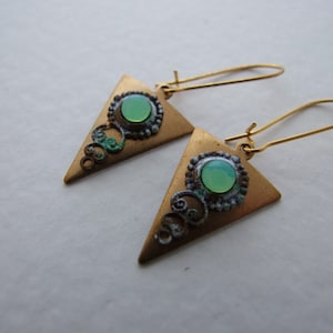 May include: A pair of gold triangle earrings with green gemstone accents and intricate filigree details.