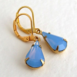May include: A pair of gold-colored leverback earrings with teardrop-shaped, light blue pendants. The pendants are faceted and set in gold-colored metal. The earrings are displayed against a white background.