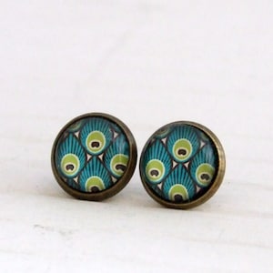 Puede incluir: Un par de pendientes de botón de bronce con un diseño de pluma de pavo real. Los pendientes presentan un patrón azul, verde y blanco.