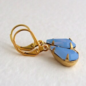 May include: A pair of gold-toned leverback earrings with teardrop-shaped, light blue gemstones. The earrings have a faceted design, and the gemstones are set in a gold-colored metal. The earrings are displayed against a white background.