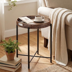 May include: A round, brown wicker side table with a black metal frame. A white coffee cup and saucer sit on the table, along with a card. A small potted fern and stack of books are nearby. The table is 24 inches tall.