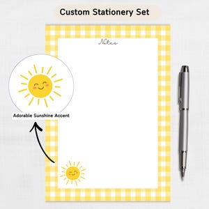 May include: Custom stationery set featuring a yellow and white gingham border. The set includes a notepad with the word "Notes" and a smiling sun graphic. A silver pen is placed next to the notepad. The text "Adorable Sunshine Accent" is also present.