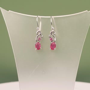 Può includere: Un paio di orecchini pendenti in argento con un design in metallo curvo, ciascuno incastonato con una piccola pietra rosa rotonda e una pietra rosa ovale più grande. Gli orecchini pendono da ganci in argento e hanno una finitura lucida.