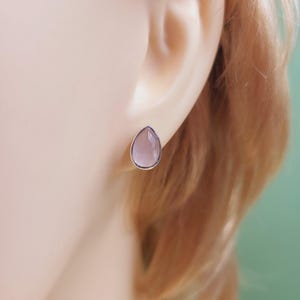 May include: A pair of silver stud earrings with a teardrop-shaped pink gemstone.