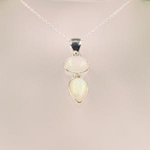 May include: A silver pendant necklace featuring two iridescent white opal stones set in polished silver. The top stone is oval-shaped, while the bottom stone is teardrop-shaped. The pendant hangs from a delicate silver chain.