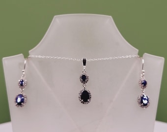 May include: A silver necklace and earrings set with two teardrop-shaped blue gemstones surrounded by smaller clear stones.