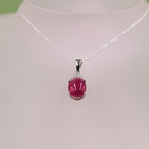 Puede incluir: Un collar de plata con un colgante de piedra roja rodeado de piedras transparentes más pequeñas.