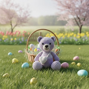 Op de afbeelding: Een gehaakte paarse teddybeer met een witte hartvormige hanger zit op groen gras naast een rieten mand vol paaseieren. Kleurrijke eieren liggen verspreid rond de beer en de mand, met bloemen en bomen op de achtergrond.