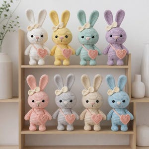 May include: A collection of eight crochet bunny dolls in various pastel colors, including white, yellow, mint green, and lavender. Each bunny has long ears, a bow, and a heart-shaped purse. They are displayed on wooden shelves.