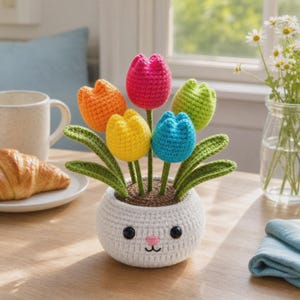 May include: A crochet flower arrangement featuring five colorful tulips in orange, pink, lime green, yellow, and blue. The flowers are set in a round, white, crocheted pot designed with a simple face, including two black eyes, a pink nose, and a mouth.