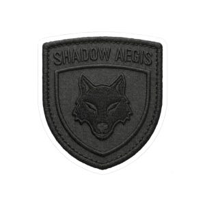 May include: Black embroidered patch with the words "SHADOW AEGIS" above a wolf's head. The patch is shield-shaped with a black border and a white background.