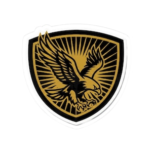 May include: A sticker featuring a stylized eagle in flight, set against a gold sunburst design within a black shield. The eagle is rendered in gold and black, creating a bold, graphic image.