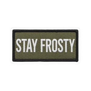 May include: A rectangular patch with the words "STAY FROSTY" in white block letters. The patch has a green background with a black border. The patch is likely an embroidered or printed design.